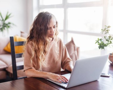 Güzel, neşeli kadın evdeki oturma odasında gümüş dizüstü bilgisayar kullanıyor.