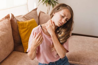 Yorgun genç bir kadın boynuna dokunuyor eklem ağrısı acıyor masaj yapıyor gergin kaslar fibromiyaljiden muzdarip uzun bilgisayar çalışmalarının ardından yanlış bir duruşla evdeki koltukta oturuyor.