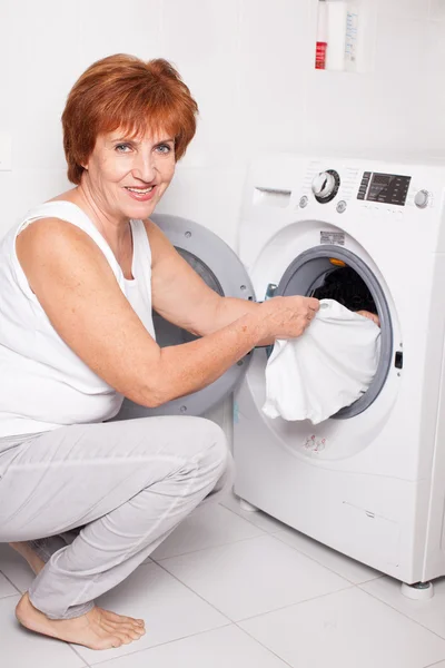 Женщина кладет одежду в стиральную машину — стоковое фото