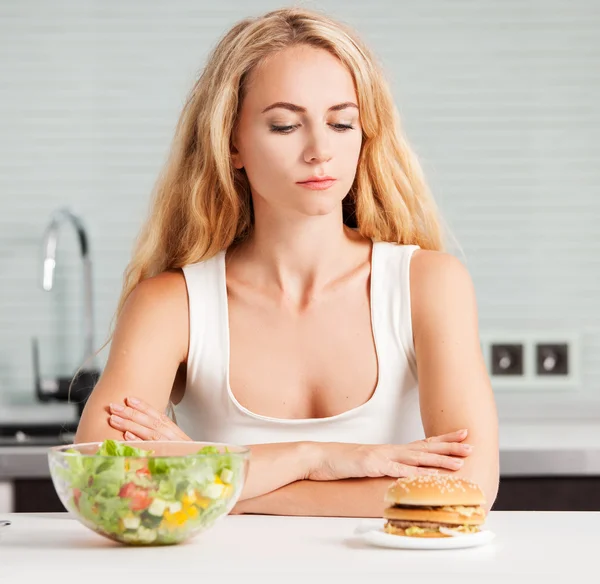 Mulher escolhe entre um alimento saudável e não saudável — Fotografia de Stock