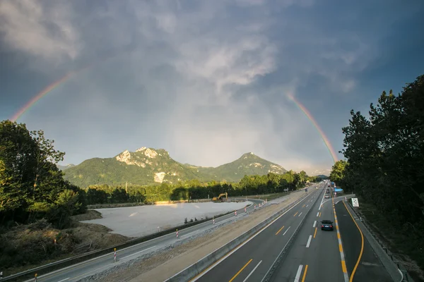 Arco-íris sobre montanhas alp e rodovia — Fotografia de Stock