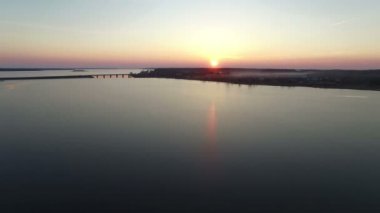 4k. Gün batımında erken ilkbaharda köprü ile büyük donmuş göl üzerinde Uçuş, havadan görünümü.