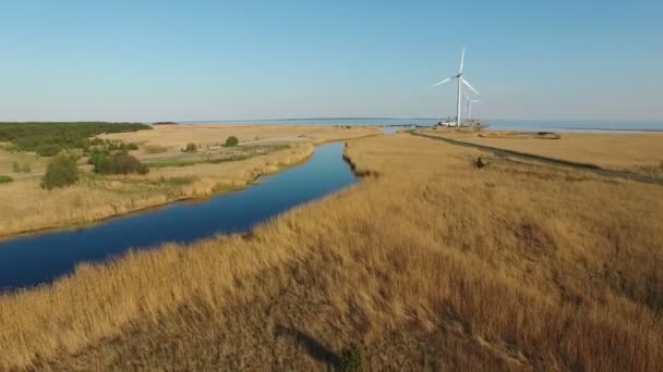 4K. Vôo baixo sobre o rio azul e campos em direção a turbinas eólicas e ao mar, vista panorâmica aérea ao pôr do sol . — Vídeo de Stock