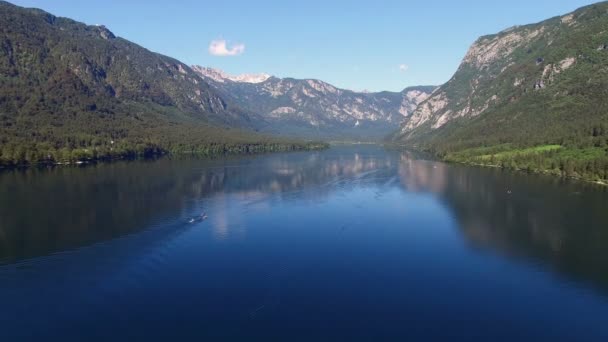 4K. Vuelo por encima del increíble lago Bohinj por la mañana. La gente está entrenando en remo. Aguas profundas azules y montañas de los Alpes Julianos. Parque Nacional de Triglav, Eslovenia, Europa . — Vídeo de stock