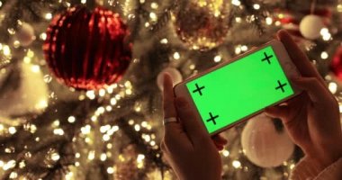 Kadın süslü Noel ağacının yanındaki akıllı telefondan yeşil ekrana bakıyor..
