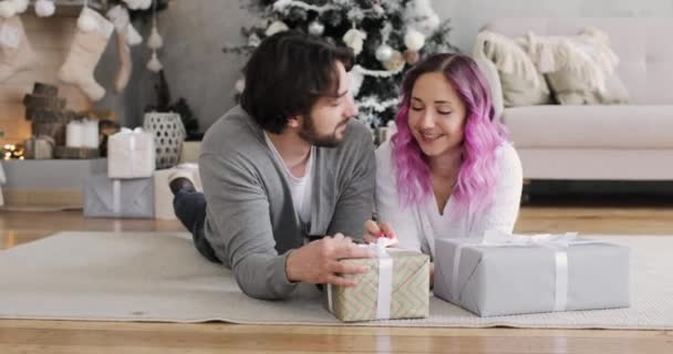 Пара чоловік і жінка лежать на підлозі розпаковують подарункові коробки на Різдво вдома . — стокове відео