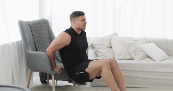 Спортивный молодой человек делает упражнения трицепс возле кресла дома, вид сбоку. — стоковое видео