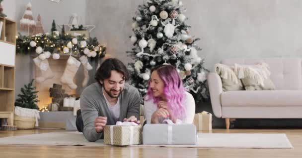Пара молодий чоловік і жінка лежать на підлозі розпаковують подарункові коробки на Різдво . — стокове відео