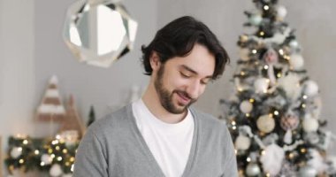 Genç mutlu adam evde Noel ağacının yanında bir hediye kutusu açıyor..