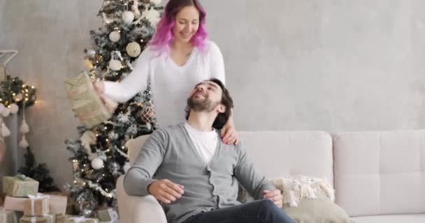 Молода жінка дарує чоловікові подарунок в інтер'єрі Нового року вдома . — стокове відео
