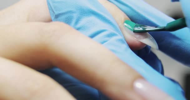 Майстер манікюру малює жіночі нігті зеленим гелем, руки крупним планом . — стокове відео