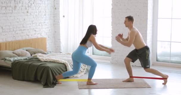 Femme et homme s'entraînent et font des exercices de jambes en utilisant des élastiques à la maison. — Video