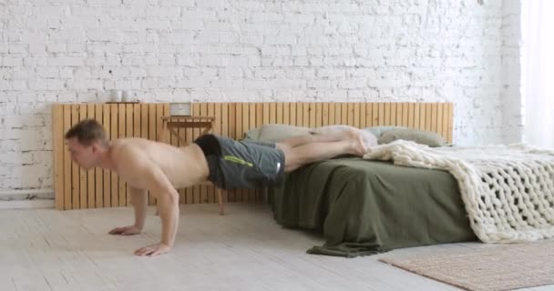 Athlétique jeune homme faisant push ups exercice avec les jambes sur le lit à la maison, vue latérale. — Video