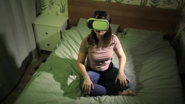 Frau sitzt in Virtual-Reality-3D-Brille im Bett und wischt mit der Hand in der Luft. — Stockvideo