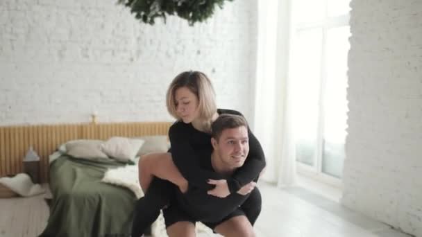 Man doing squat exercise hilding woman on his back instead of a barbell at home. — Stock Video