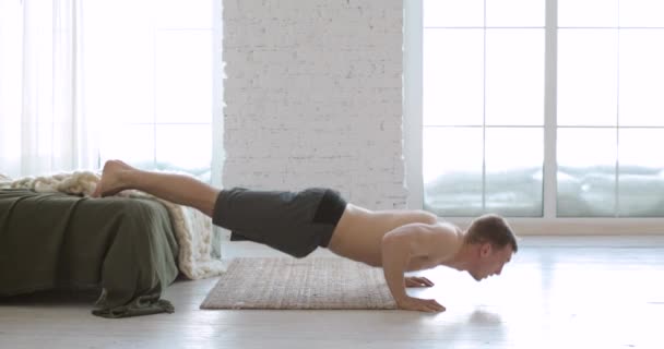 Sportowy młody człowiek robi pompki ćwiczenia z nogami na łóżku w domu, widok z boku. — Wideo stockowe