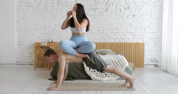 Мужчина делает статические упражнения доски дома с женщиной, сидящей наверху на спине. — стоковое видео