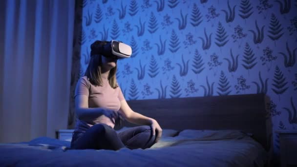 Kvinna sitter i sängen i virtuell verklighet 3D-glasögon och lära sig något. — Stockvideo