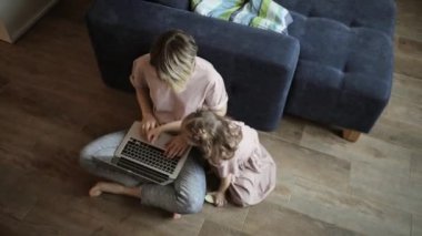 Anne küçük oğluna laptopta çalışmayı öğretiyor. Evde yerde oturuyor..