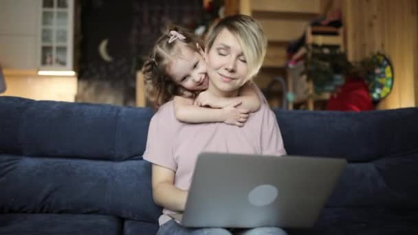 Mam probeert te werken op laptop met haar dochter knuffelen haar in de woonkamer. — Stockvideo