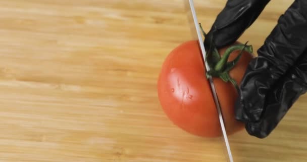 Кухарі руками в чорних рукавичках нарізають свіжий помідор на шматки на дерев'яній дошці . — стокове відео