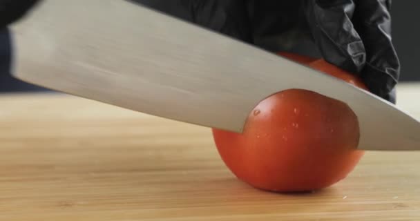 Kookt handen in zwarte handschoenen snijden verse tomaat in plakjes op houten bord. — Stockvideo