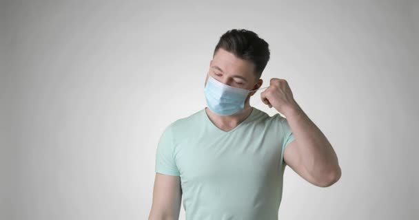 Sakallı adam tıbbi maskeyi çıkarır ve gri arka planda derin bir nefes alır.. — Stok video