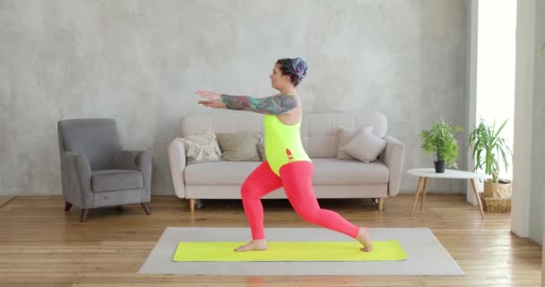 Gruba kobieta przybysz robi przysiady w lunges ćwiczenia stojąc na macie w domu. — Wideo stockowe
