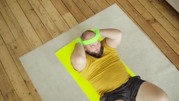 Tyk træt mand i gul sportstøj gør abs motion crunches liggende på måtten. – Stock-video