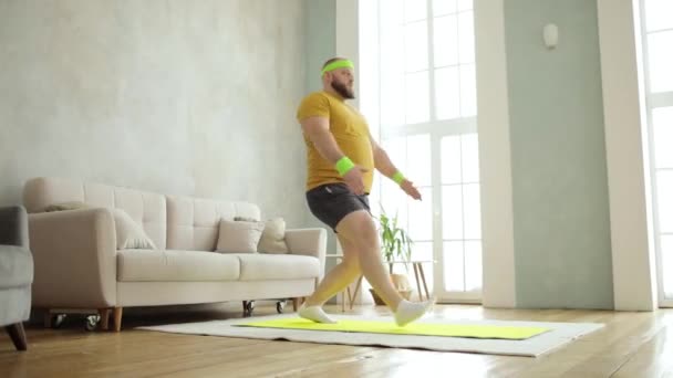 Plump man gör knäböj i lungorna motion med händerna upp stående på mattan hemma. — Stockvideo