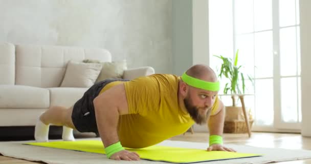 Dicker Mann in gelber Sportbekleidung macht Sport-Liegestütze auf Matte zu Hause.. — Stockvideo