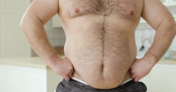 Мужчина без рубашки с избыточным весом, с опущенным желудком, чешет животик, вид спереди. — стоковое видео