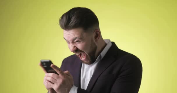 Šťastný mladý muž v kancelářském obleku při pohledu na smartphone dělá vítězný gesto. — Stock video