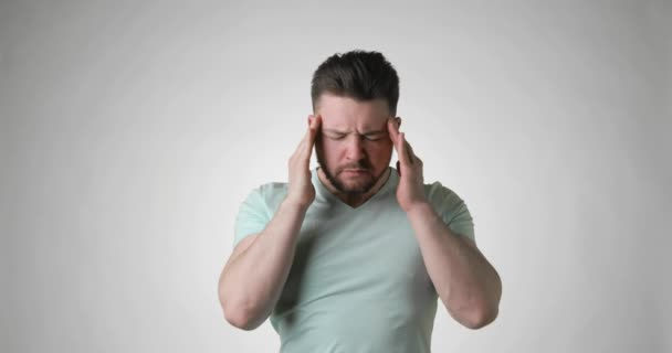 Sjuk skäggig ung man i grön t-shirt sätta händerna på huvudet har huvudvärk. — Stockvideo