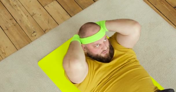 Fet man i gula sportkläder gör abs motion crunches hemma liggande på mattan. — Stockvideo