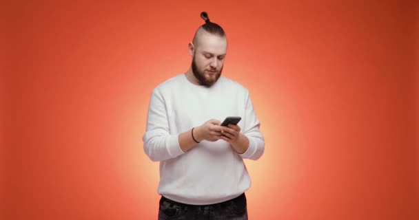 Alegre joven barbudo está mirando en el teléfono inteligente haciendo gesto ganador. — Vídeos de Stock