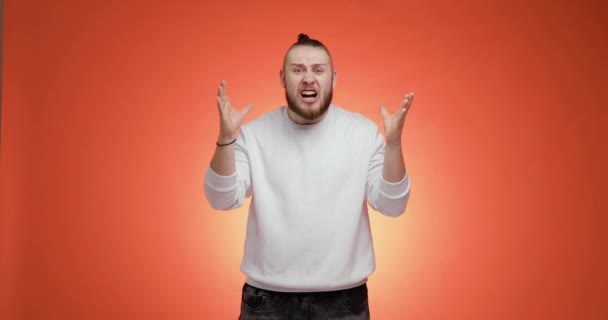 Surprised bearded young man with hair tail says what the fuck on red background. — Vídeo de Stock