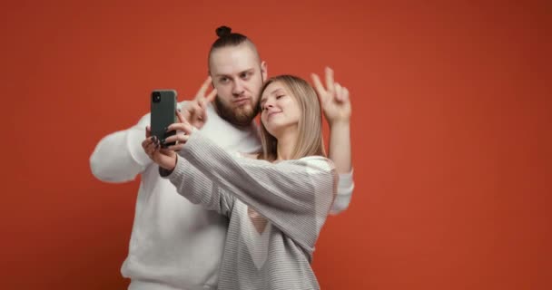 Щаслива пара жінка робить селфі разом, використовуючи смартфон на червоному тлі . — стокове відео