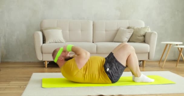 Fat man newcomer in sport in sportswear doing abs exercise at home lying on mat. — Stock Video