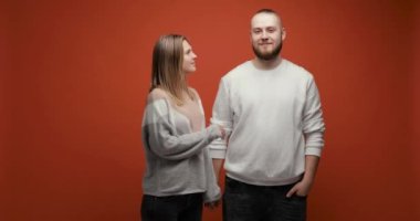 Sakallı genç adam ve kadın kırmızı arka planda öpüşüyorlar..