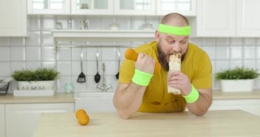 Danar yiyen şişman adam masada oturuyor ve halterle el egzersizi yapıyor..