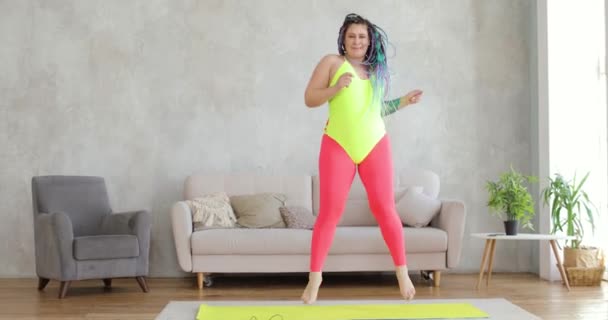 Vet gelukkig vrouw in helder sportkleding is emotioneel dansen op mat thuis. — Stockvideo