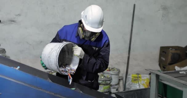 Ein Mann in Uniform schüttet gebrauchte Batterien aus einem Eimer auf ein bewegliches Förderband. — Stockvideo