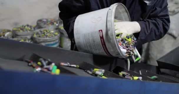 Pemandangan tangan orang berseragam dan sarung tangan menuang baterai bekas dari ember ke sabuk konveyor yang bergerak. — Stok Video