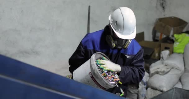 Ein Mann in Uniform schüttet gebrauchte Batterien aus einem Eimer auf ein bewegliches Förderband. — Stockvideo