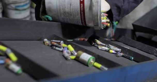 Vista de las manos de la persona en uniforme y guantes vertiendo las baterías usadas del cubo en una cinta transportadora en movimiento. — Vídeo de stock