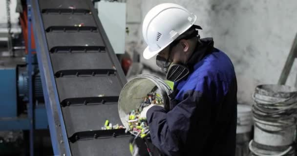 Ein Mann in Uniform schüttet gebrauchte Batterien aus einem Eimer auf ein bewegliches Förderband. — Stockvideo