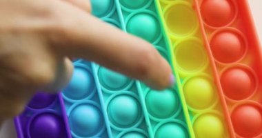 Eller stres önleyici, pop it oyuncağıyla oynar. Gökkuşağı duyusal kıpırdaması beyaz arka planda izole edilmiş. Yeni moda silikon oyuncak.