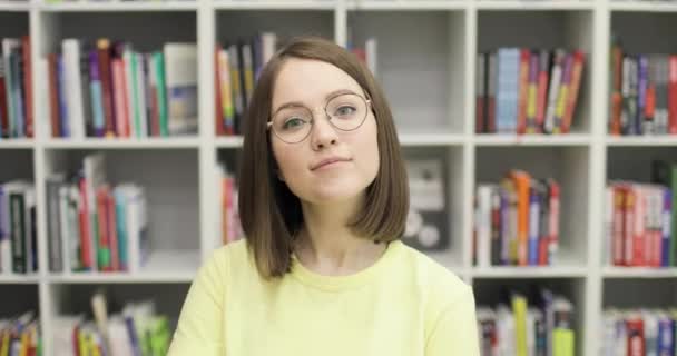 Jovem bela estudante europeia usando óculos sorrindo alegremente posando para câmera na biblioteca da faculdade. — Vídeo de Stock