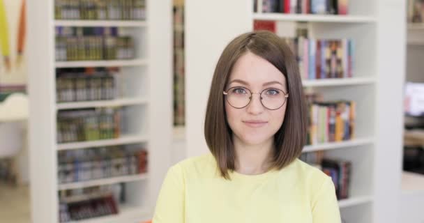 Jovem bela estudante europeia usando óculos sorrindo alegremente posando para câmera na biblioteca da faculdade. — Vídeo de Stock